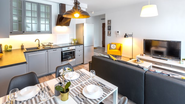 A modern kitchen with grey cabinets, a built-in oven, and a dining area with a striped tablecloth and black chairs. - Friendhouse Apartments - Train Station Area (Kraków)