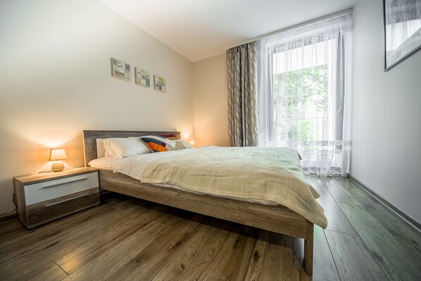 A bedroom with a wooden bed, a nightstand with a lamp, and a window with curtains.