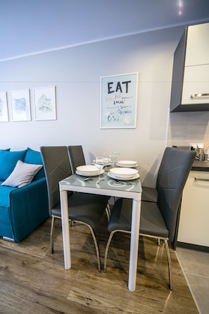 A dining area with a table set for four, a teal sofa, and a kitchen in the background. - FriendHouse Apartments – Krowoderska (Kraków)