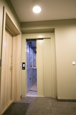 A hallway with a wooden door, a digital elevator control panel, and a tiled floor.