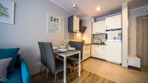 Een kleine keuken met moderne apparaten, een eethoek met tafel en stoelen, en een blauwgroene bank.