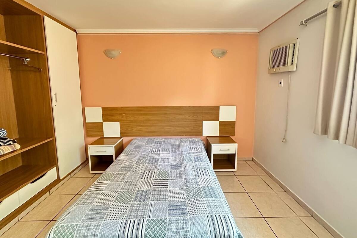 A bedroom with a bed, bedside tables, a wardrobe, and an air conditioning unit.