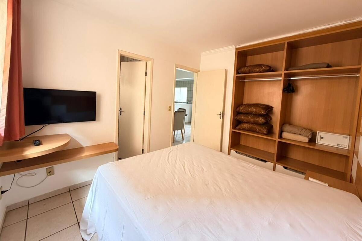 A bedroom with a bed, a TV, a wooden wardrobe, and a desk.