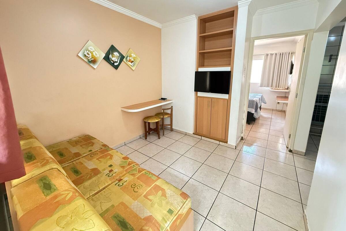 A living room with a sofa, a TV, and a small table. There are three wall-mounted pictures and a door leading to another room.