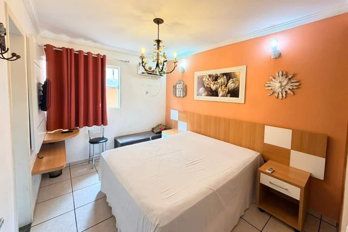 A bedroom with a bed, a nightstand, a chair, a desk, a chandelier, and a wall clock.