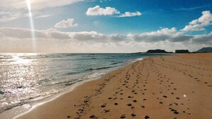 Una playa con huellas que conducen al agua, un cielo despejado y edificios a lo lejos.