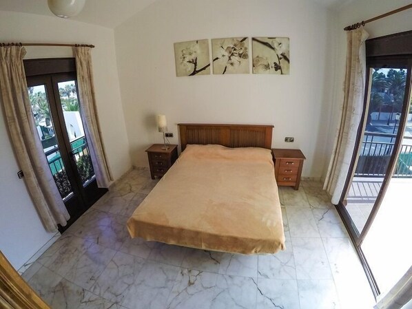 Un dormitorio con una cama grande, una mesita de noche, una lámpara y vistas al exterior a través de un ventanal.