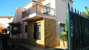 Una casa de dos pisos con balcón, fachada de piedra y entrada protegida por una reja.