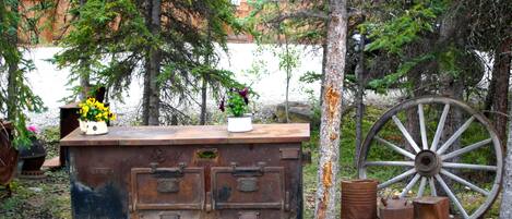 A rustic wooden bench with a planter, surrounded by trees and a large wooden wheel.