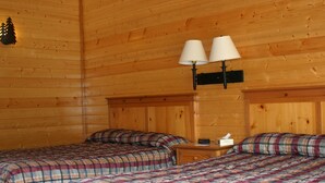 Een houten kamer met twee bedden, elk voorzien van geruit beddengoed, een nachtkastje met een lamp en een houten hoofdbord.