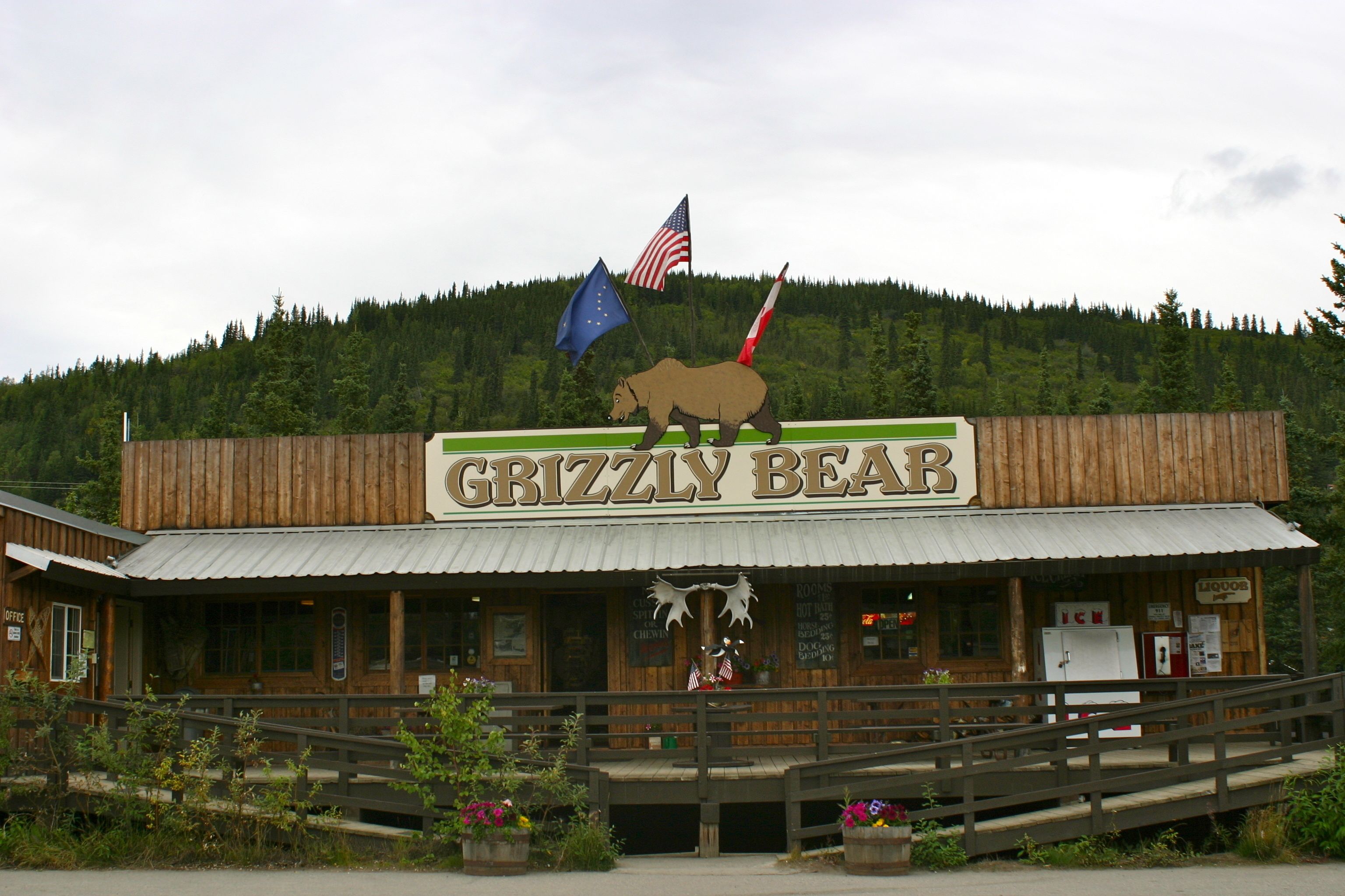 Un edificio rústico llamado 'Grizzly Bear' con fachada de madera, una cabeza de alce montada y banderas.