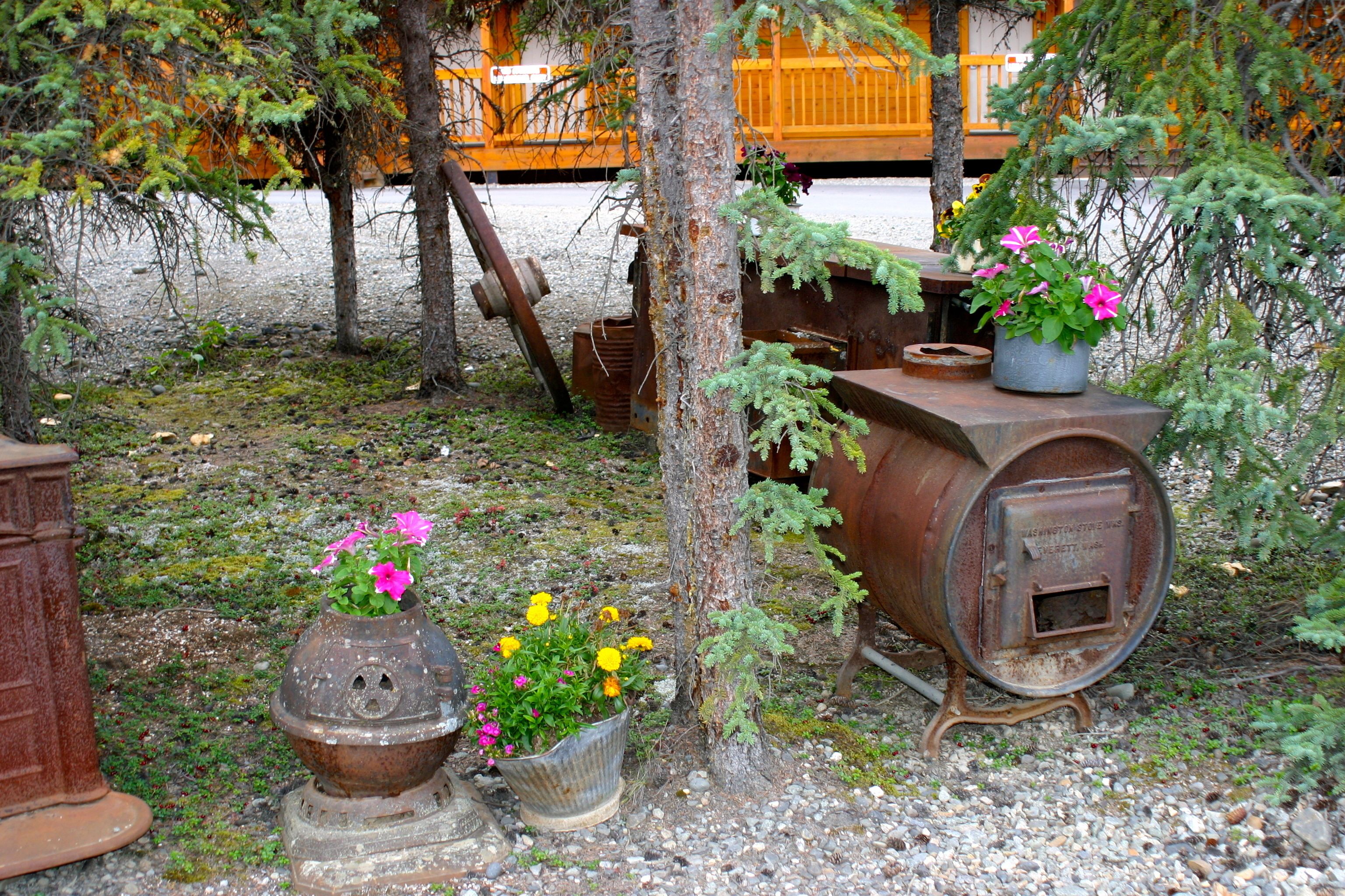 Un décor extérieur rustique comprenant un tonneau en bois, des plantes en pot et une structure métallique.