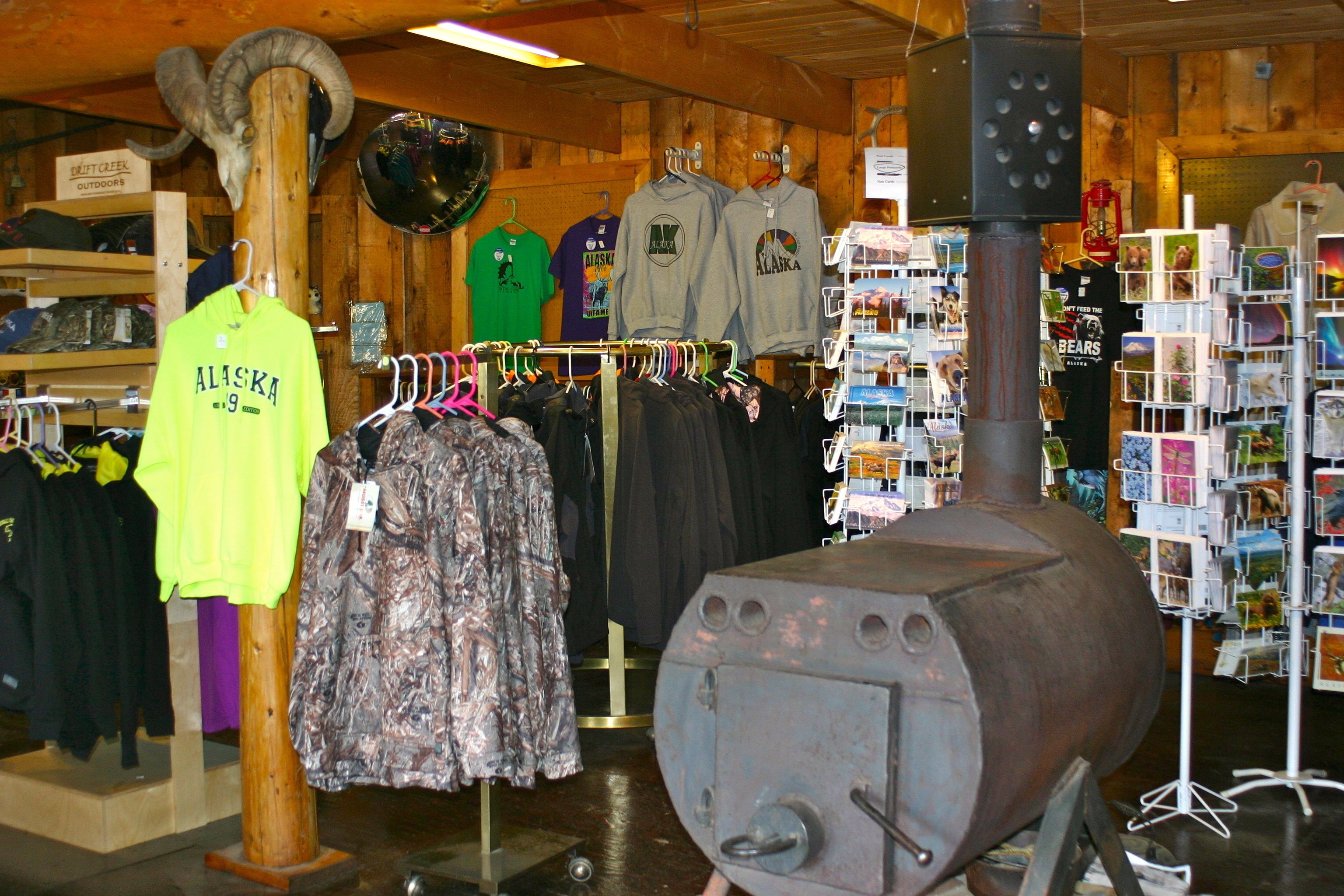 A rustic interior with wooden walls, a large metal stove, and various clothing items on racks.