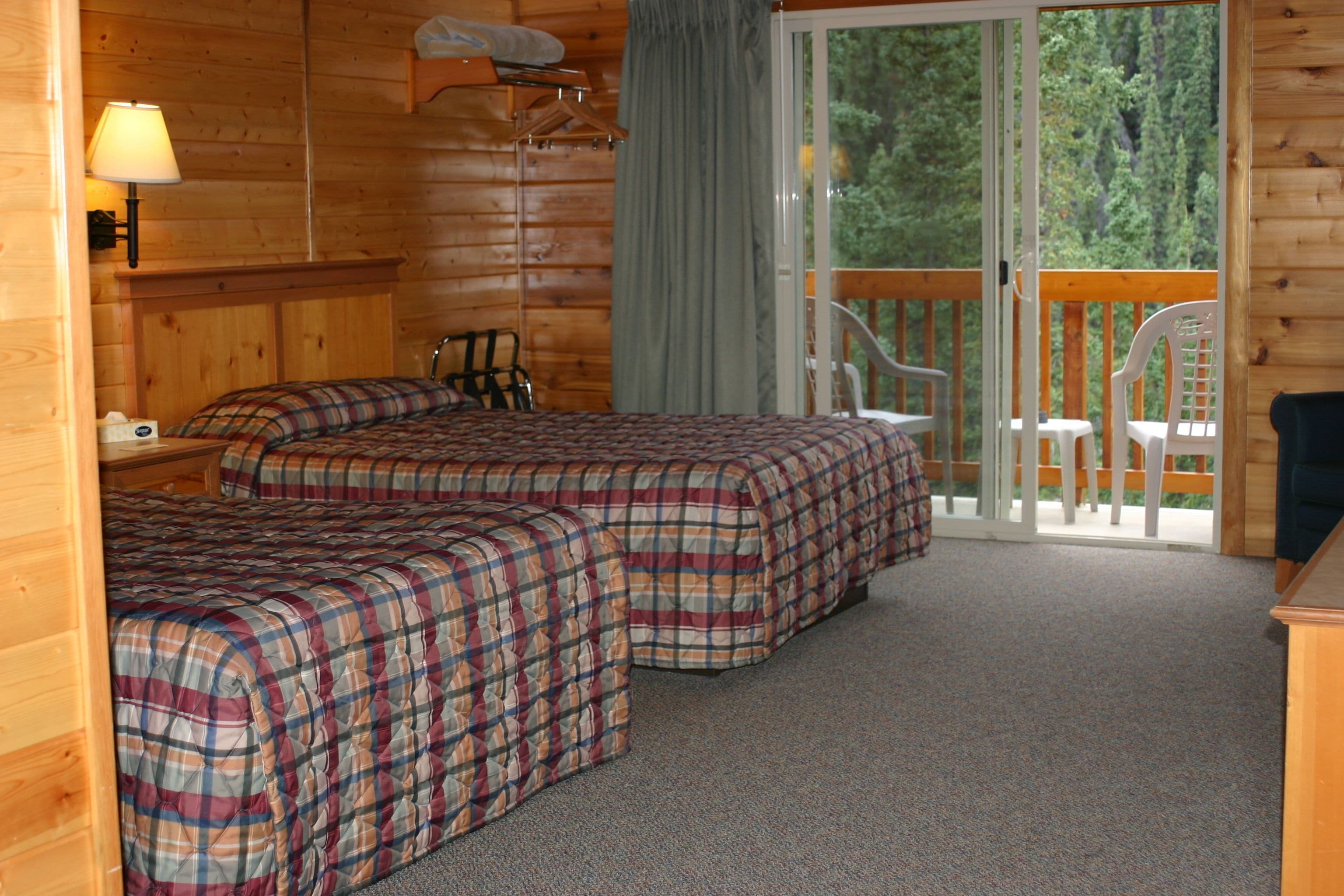 A cabin with two beds, a balcony with chairs, and a wooden interior.