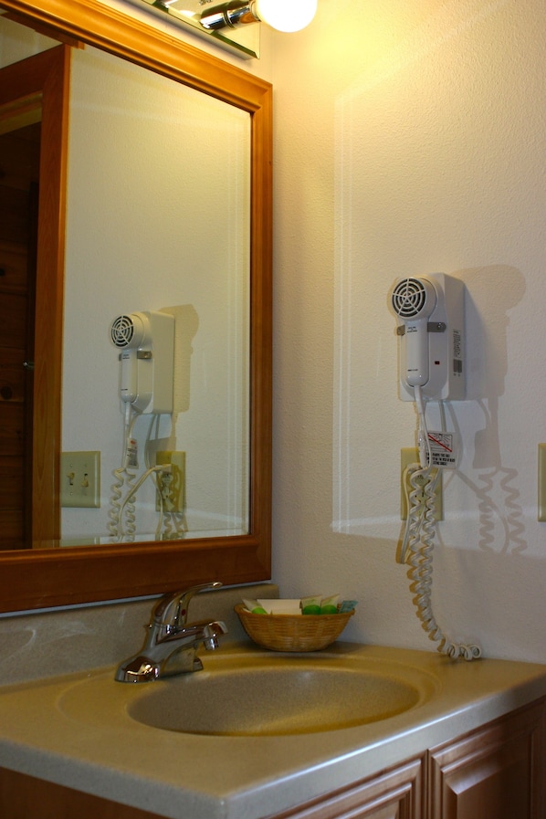 Un bagno con lavandino, specchio e asciugacapelli fissato al muro.