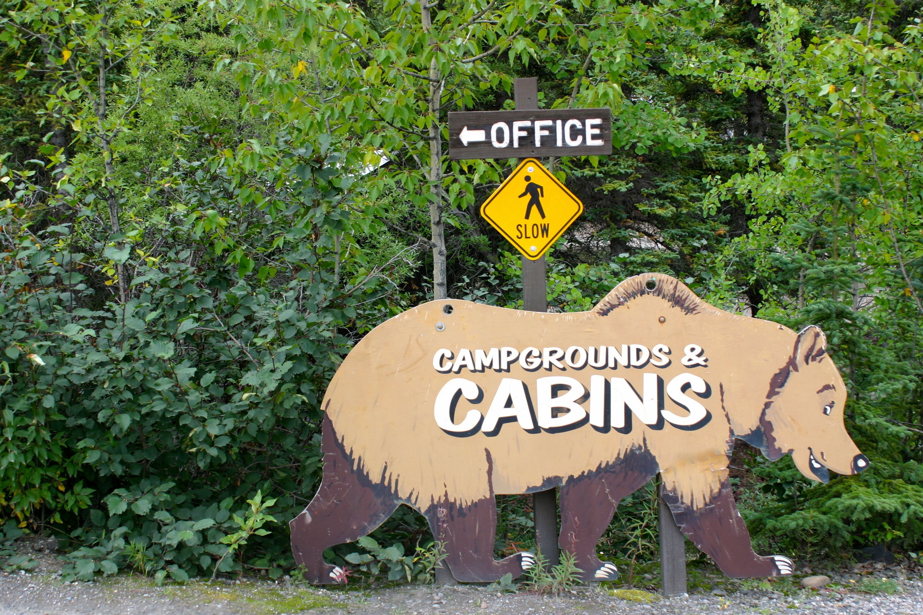 A wooden sign with a bear design and text indicating "CAMPGROUNDS & CABINS" and an arrow pointing left for the office.