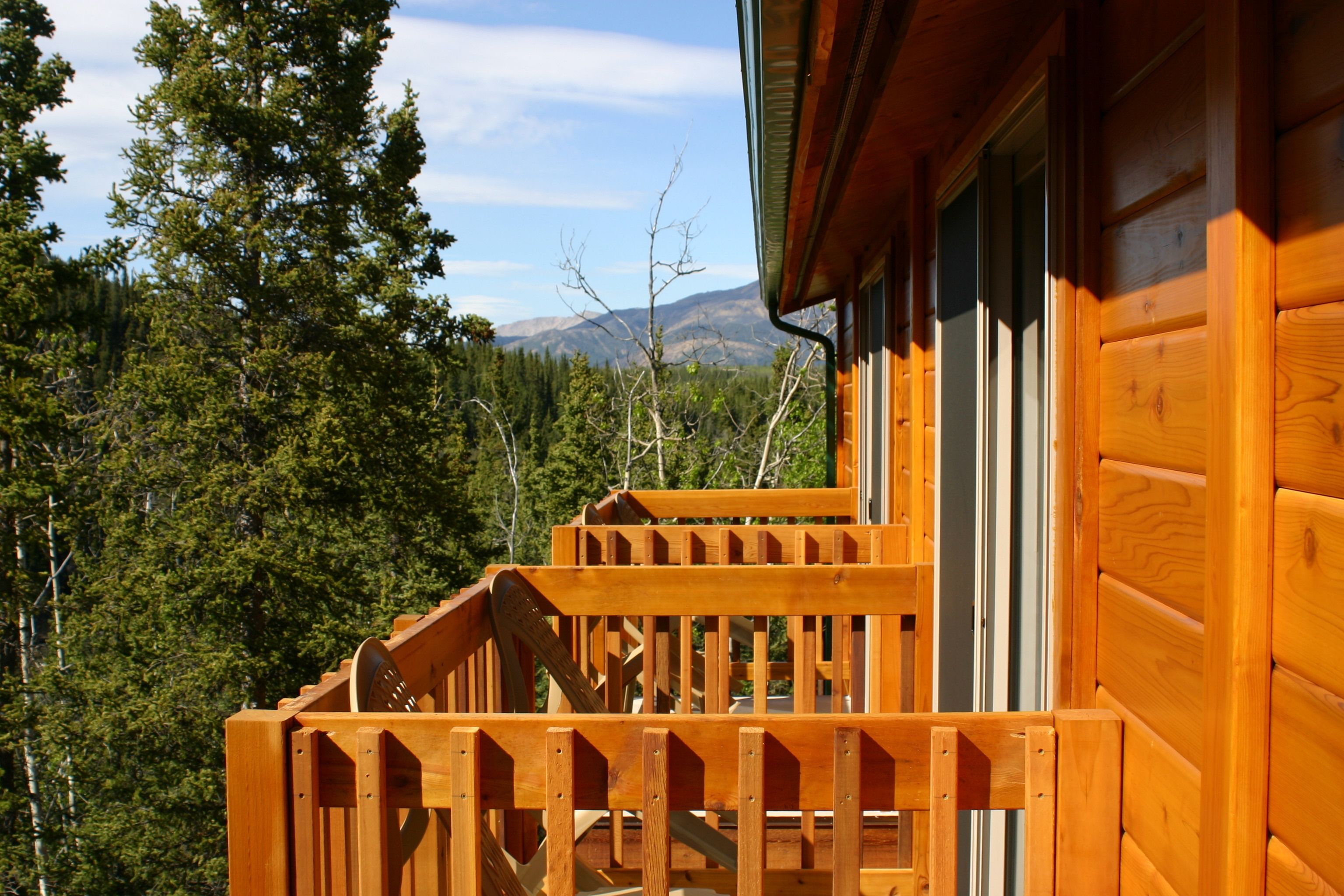A wooden cabin with a balcony overlooking a forested area and mountains.