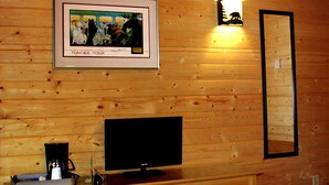 Houten cabin inrichting met een lijstfoto van een tocht door de toendra, een flatscreen televisie, een koffiezetapparaat en een wandlamp.