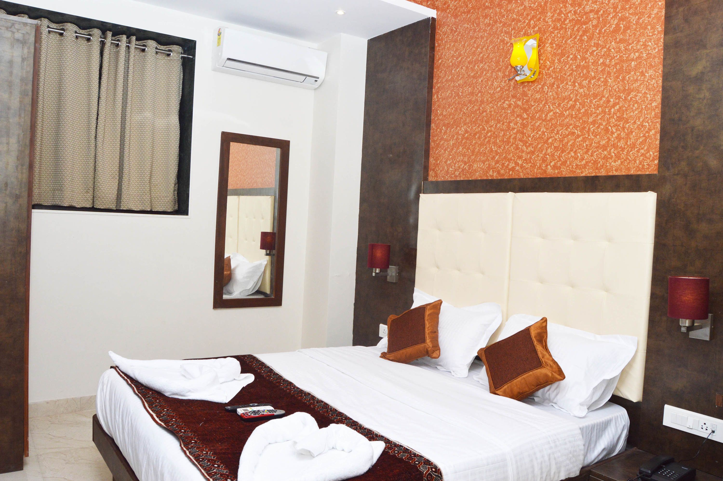 A hotel room with a large bed, a mirror, a wall-mounted air conditioner, and a decorative wall panel.