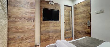 A hotel room with a large bed, wooden panel walls, a mounted TV, and a trash bin.
