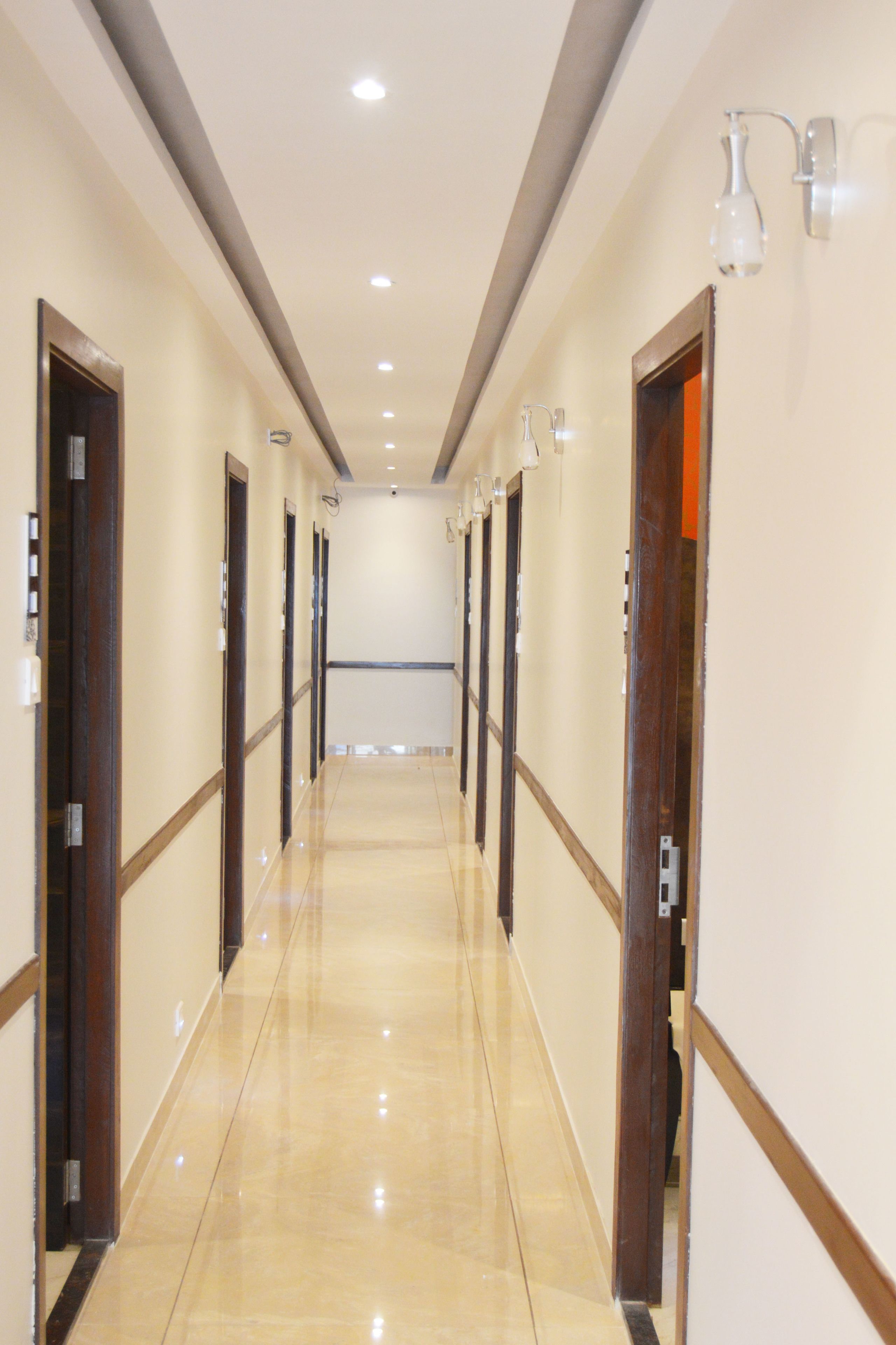 A long, well-lit hallway with wooden doors and light fixtures on the walls.