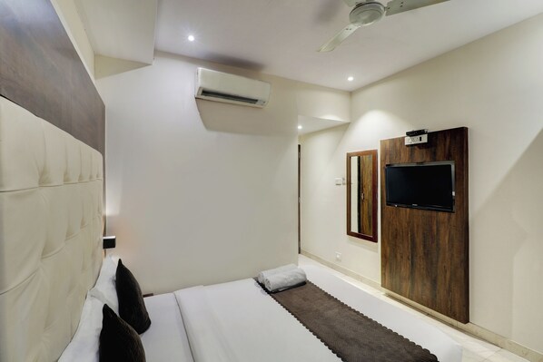Una habitación de hotel moderna con una cama grande, un equipo de aire acondicionado, un televisor de pantalla plana montado en un panel de madera y un ventilador de techo.
