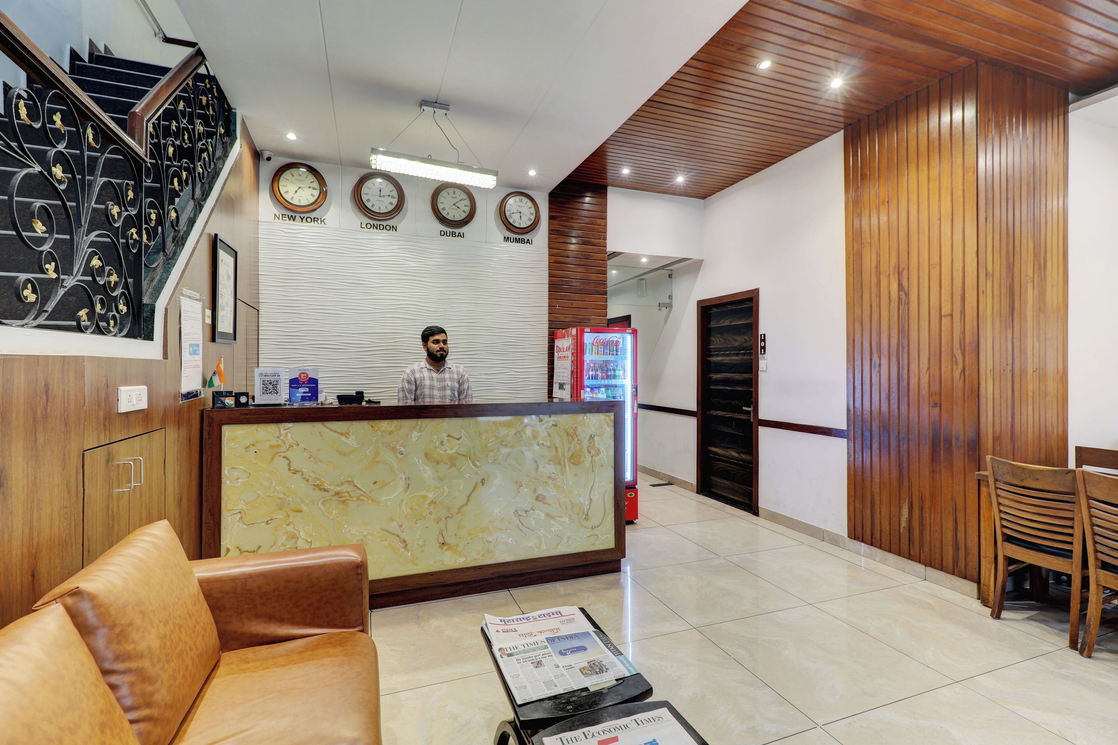 A reception area with a marble counter, a clock displaying time in four cities, a staircase, and a wooden wall.