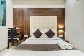 A bedroom with a tufted headboard, two bedside lamps, a bed with white bedding, a brown throw blanket, and a rolled towel on the bed. - Hotel AK International (Mumbai)
