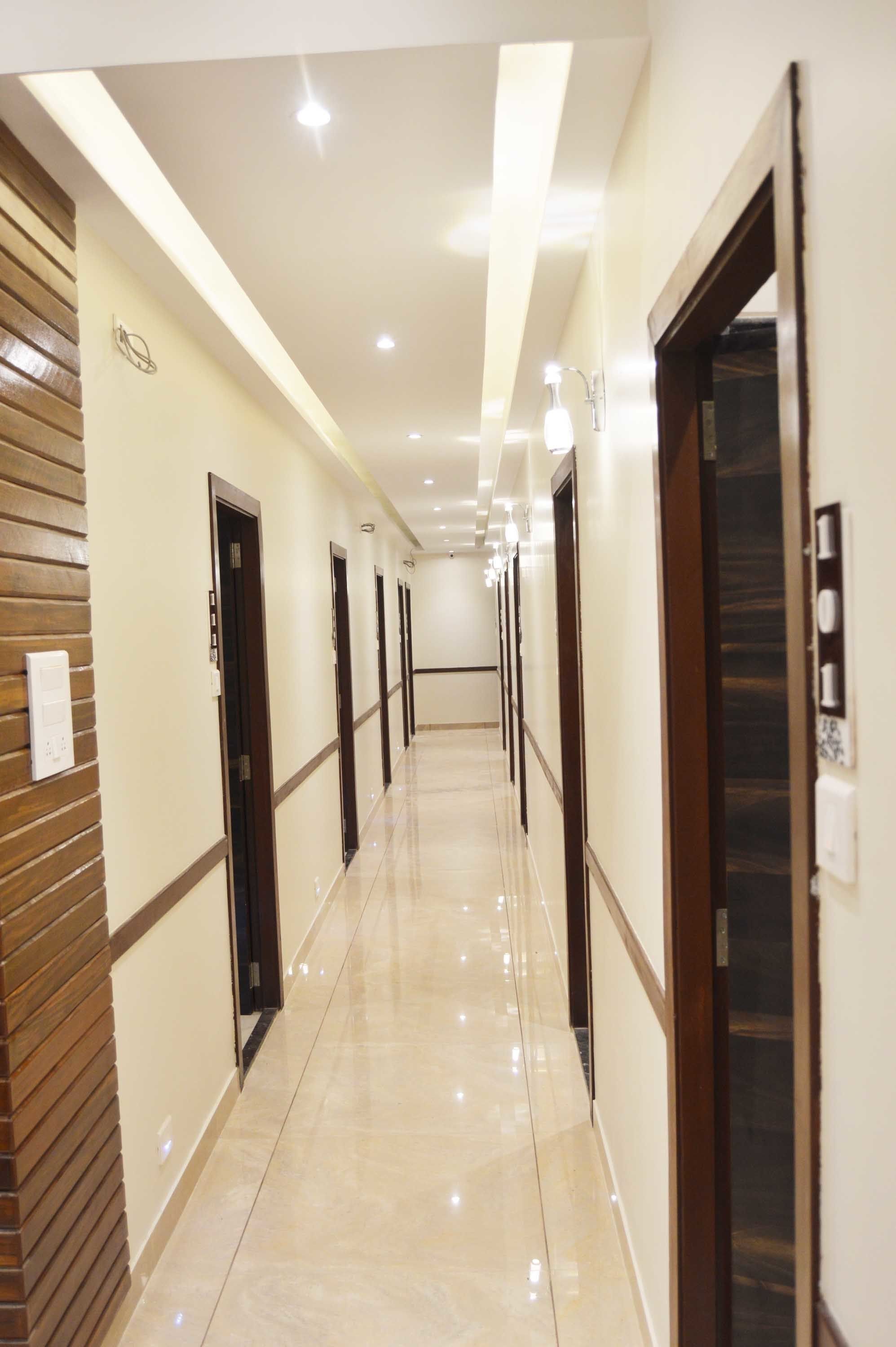 A hotel corridor with a polished floor, wooden paneling on one side, and doors leading to rooms.