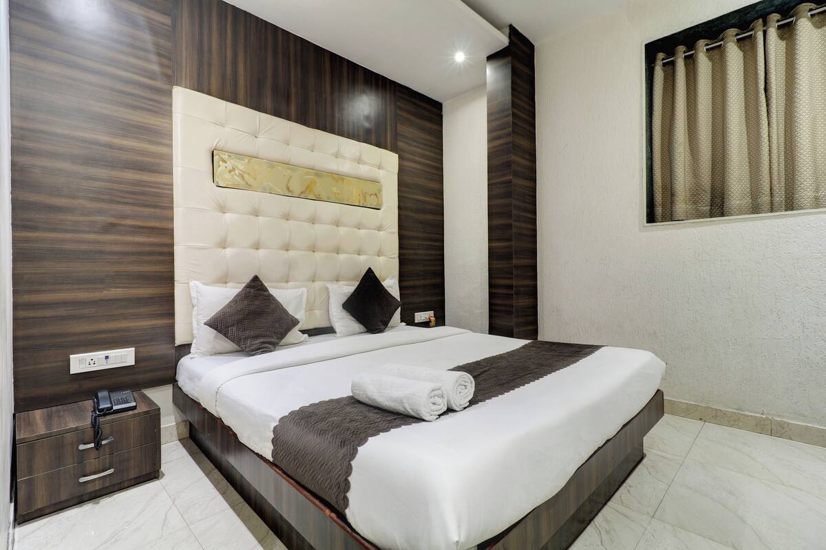 A neatly made bed with a white and gray bedspread, a headboard with a decorative panel, and a bedside table with a phone.