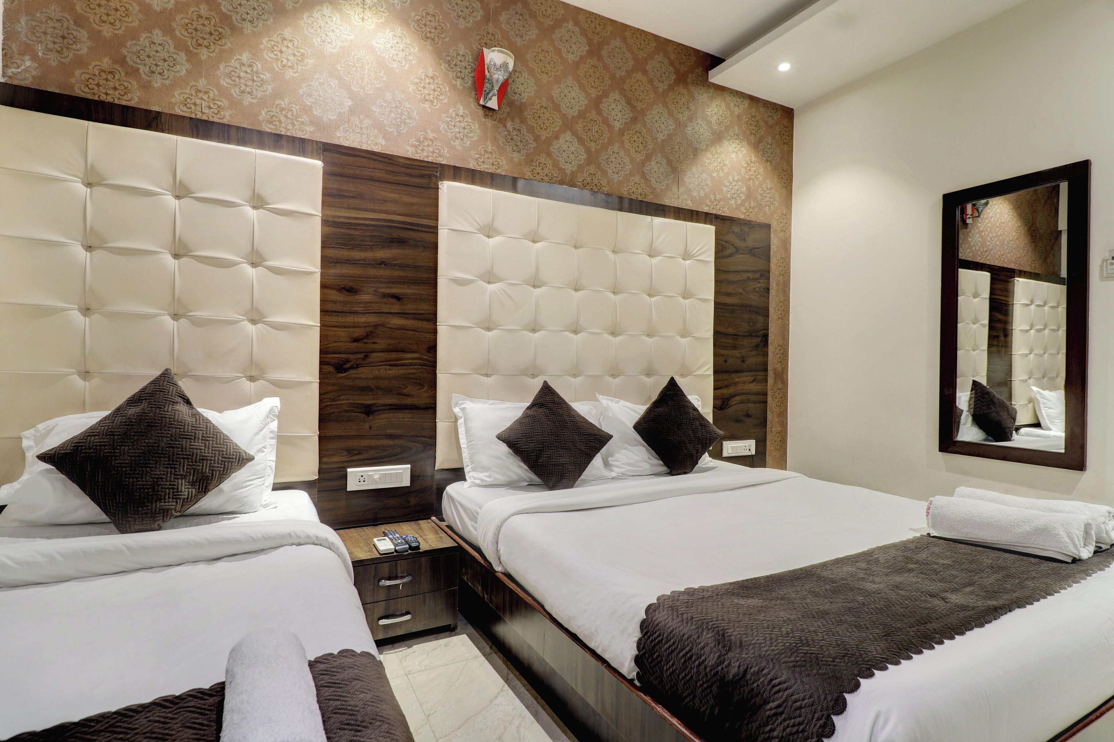 A hotel room with two beds, wooden headboards, a mirror, and a small bedside table with a lamp.