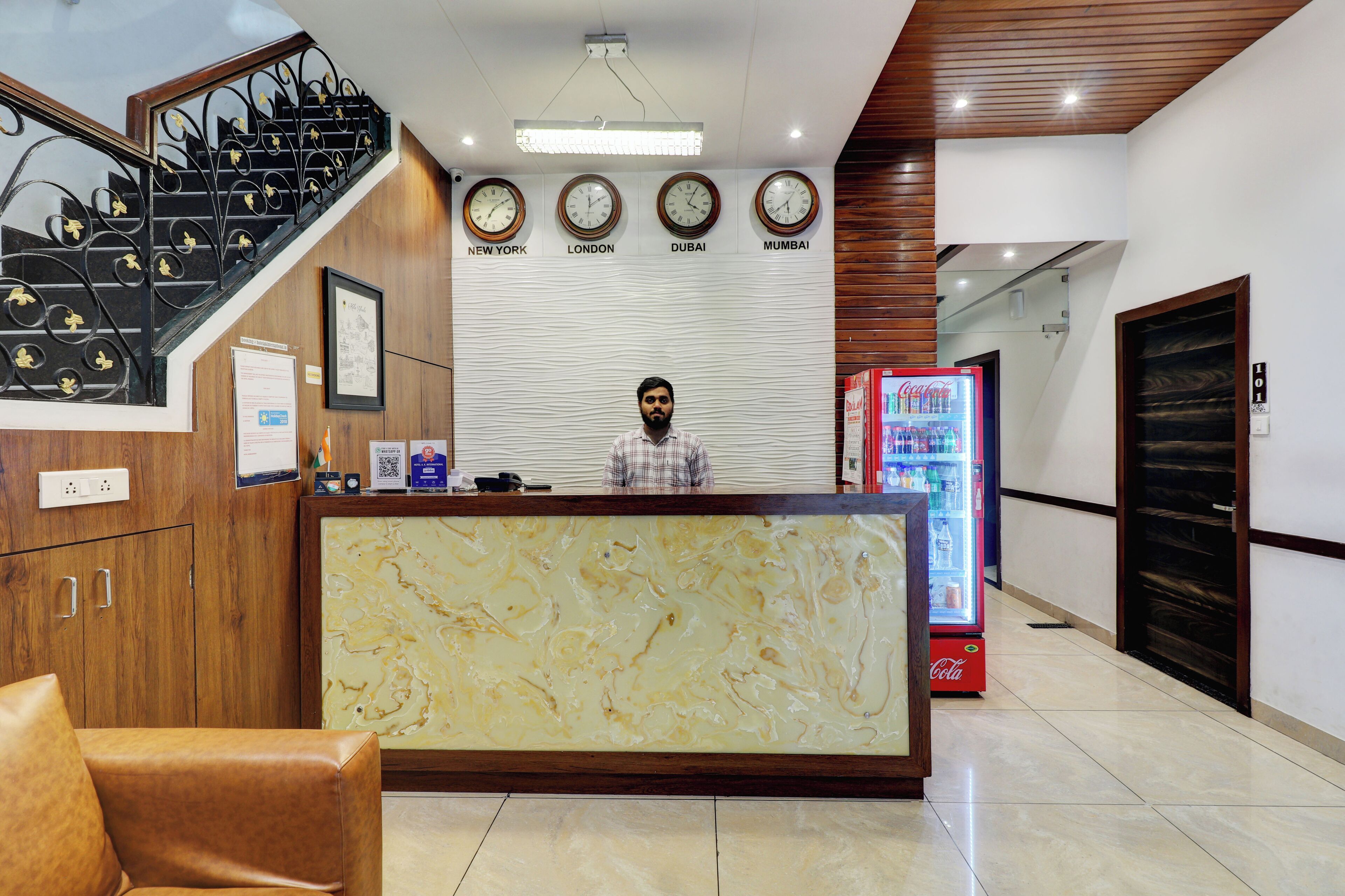A reception area with a marble counter, a Coca-Cola refrigerator, and clocks displaying times for New York, London, Dubai, and Mumbai.
