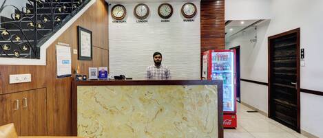 A reception area with a marble counter, a Coca-Cola refrigerator, and clocks displaying times for New York, London, Dubai, and Mumbai.
