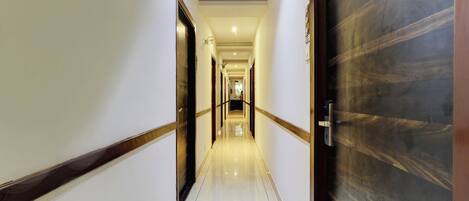 Un long couloir étroit, typique d’un hôtel, avec un sol ciré, des boiseries et une grande porte en bois sur le côté droit.