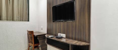 A small room with a TV mounted on the wall, a wooden chair, and a desk with a power strip.
