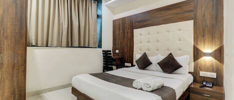 A bedroom with a large bed, wooden headboard, bedside tables, and a window with curtains.