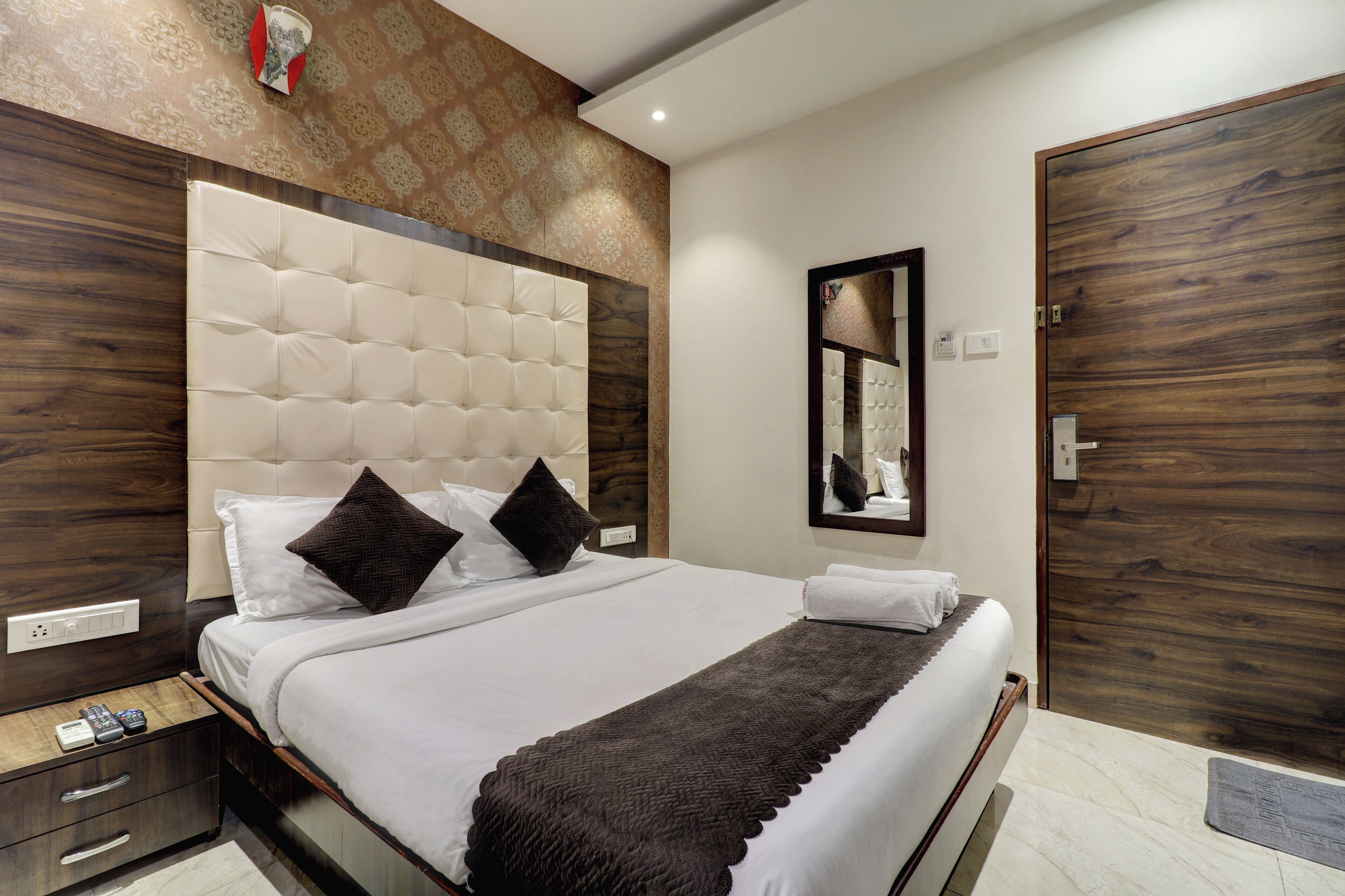 A neatly made bed with a tufted headboard, a bedside table with a drawer, and a wooden door.