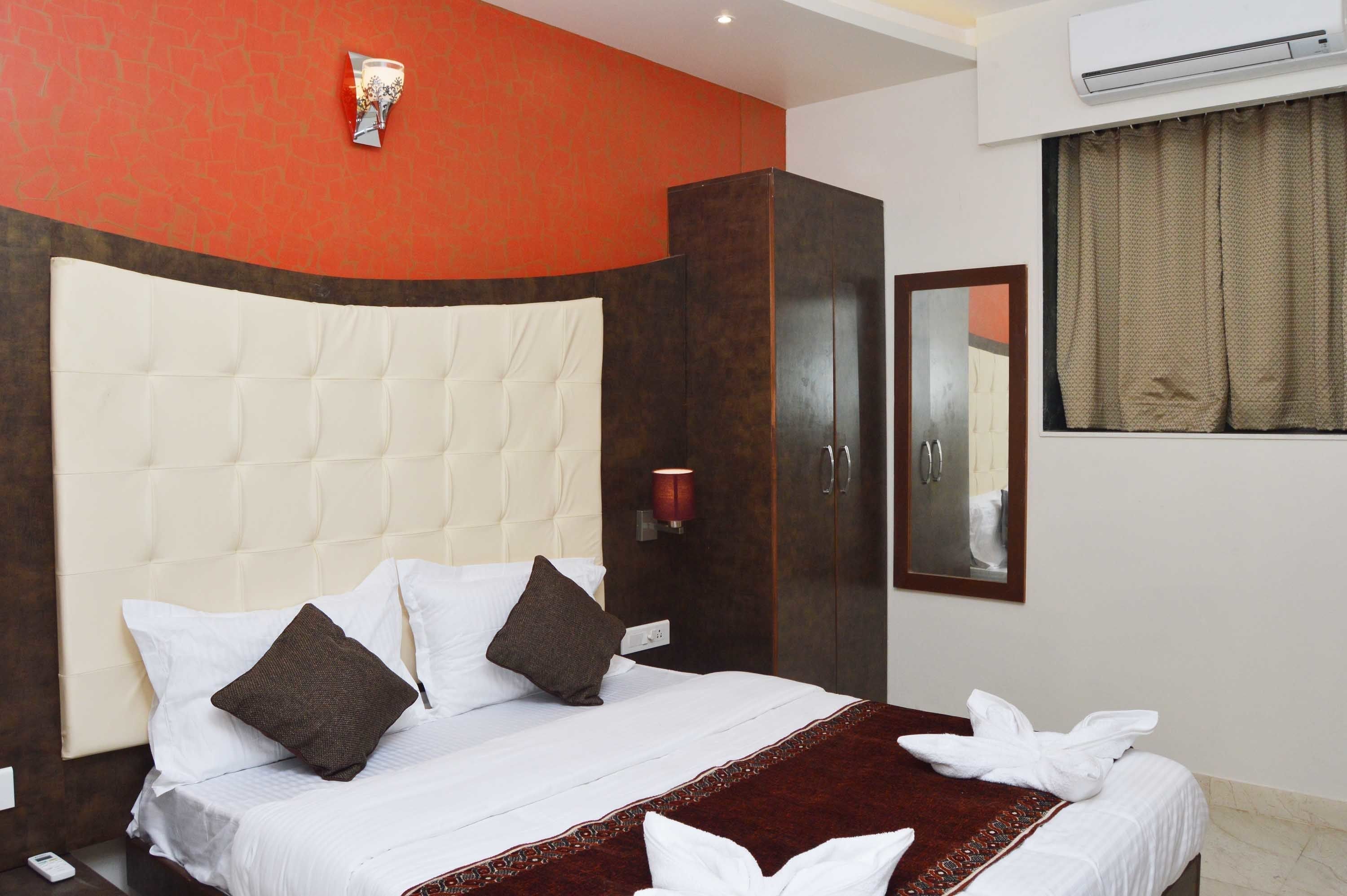 A hotel room with a large bed, a wardrobe, a mirror, and an air conditioning unit.