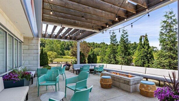 An outdoor patio with green chairs, a fire pit, and a seating area with a view of the surrounding greenery.