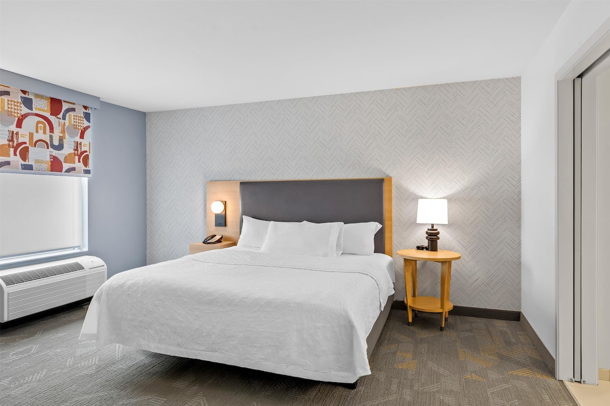 Ein Hotelzimmer mit einem großen Bett, einem Nachttisch mit Lampe, einem an der Wand montierten Telefon und einem Heizgerät.