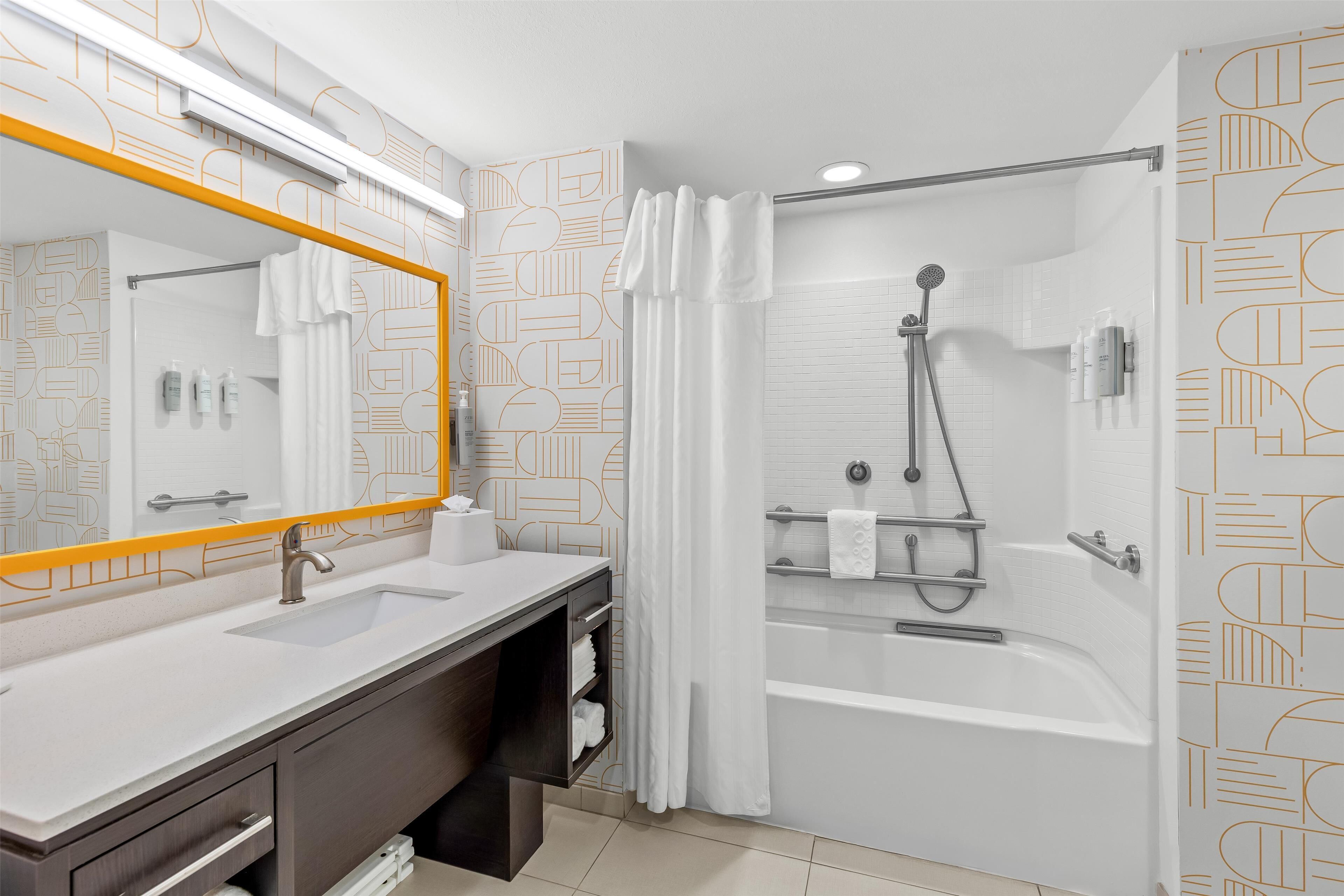 Un baño moderno con un lavamanos blanco, tocador oscuro y ducha a ras de suelo con puerta de cristal.