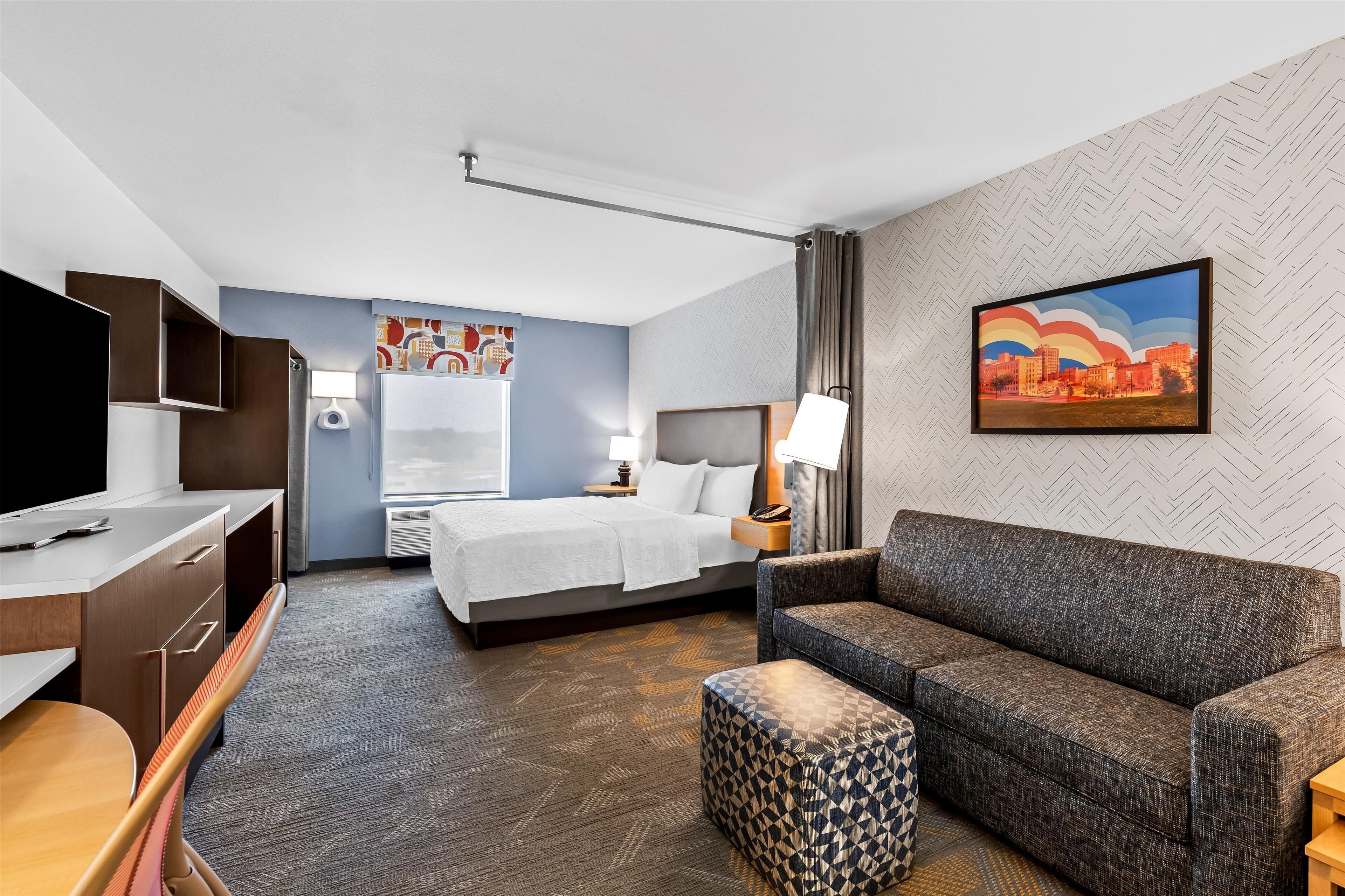 A hotel room with a bed, a sofa, a desk, and a TV.