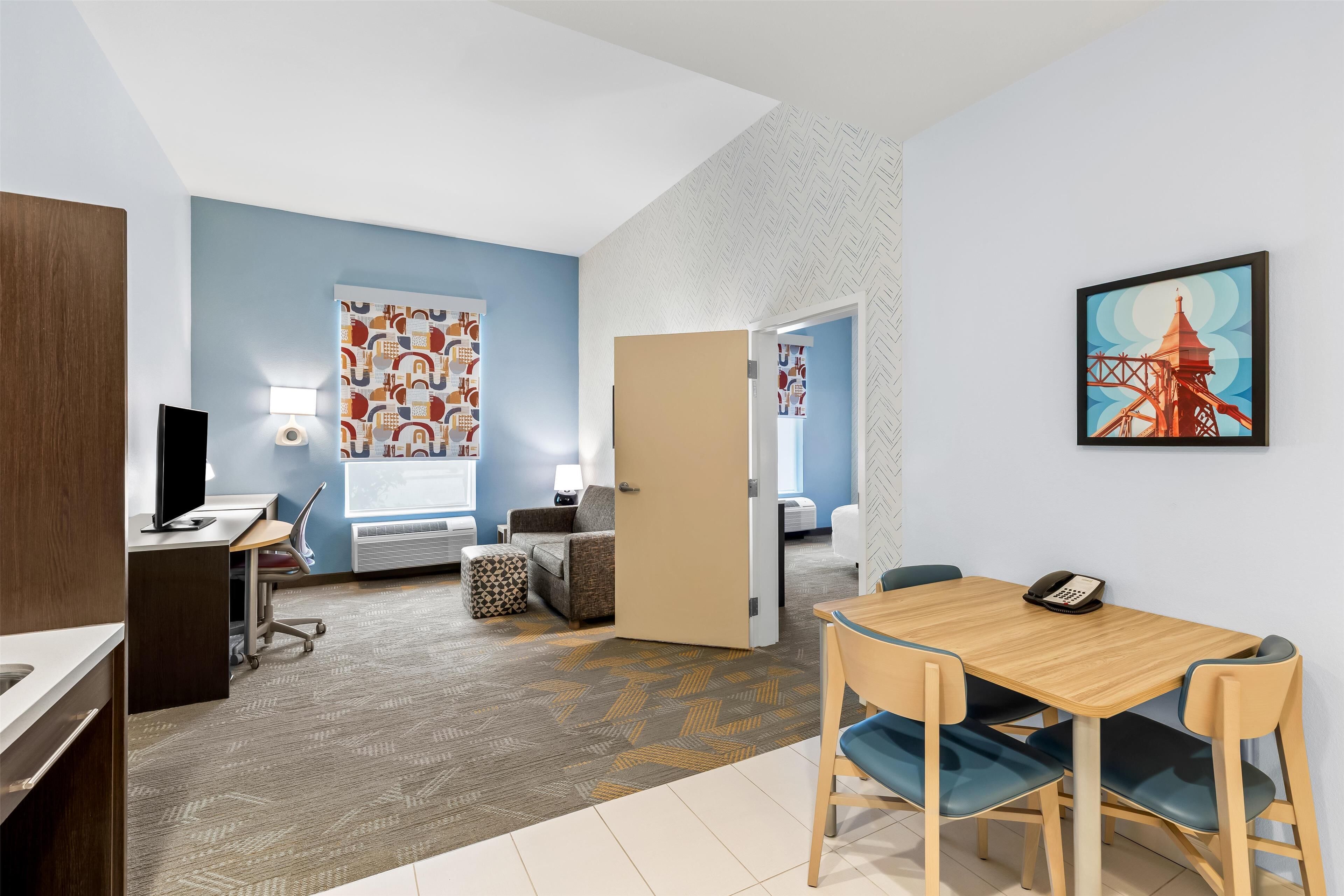 Habitación de hotel con escritorio, silla y cama. Se ve una puerta que conduce a otra habitación.