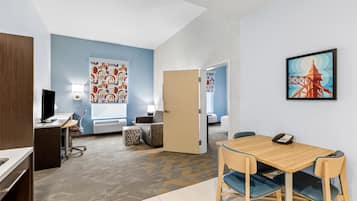 Habitación de hotel con escritorio, silla y cama. Se ve una puerta que conduce a otra habitación.