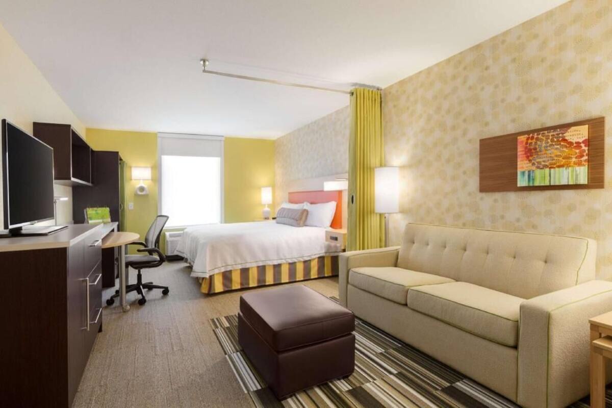 Ein Hotelzimmer mit einem Bett, einem Sofa, einem Schreibtisch mit Computer, einem Sessel und einem Fernseher.