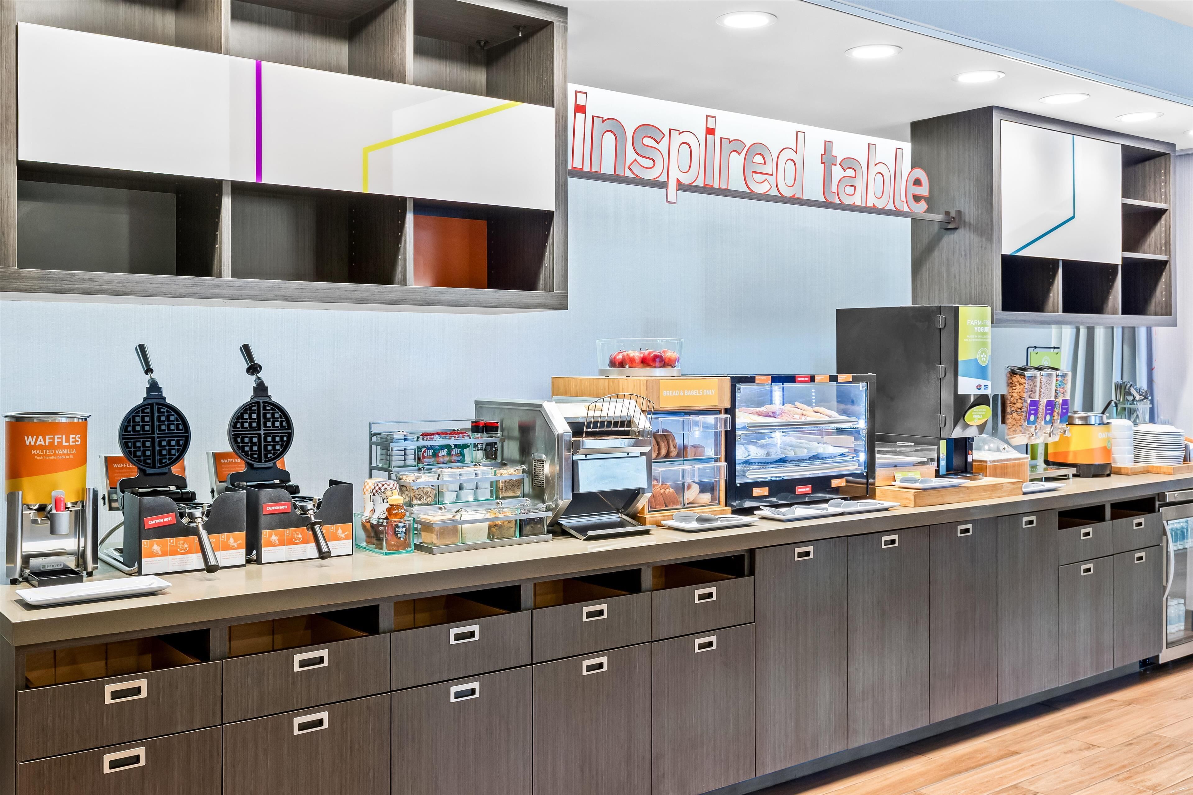 A breakfast bar with waffle makers, a sign reading 'inspired table,' and various food items.