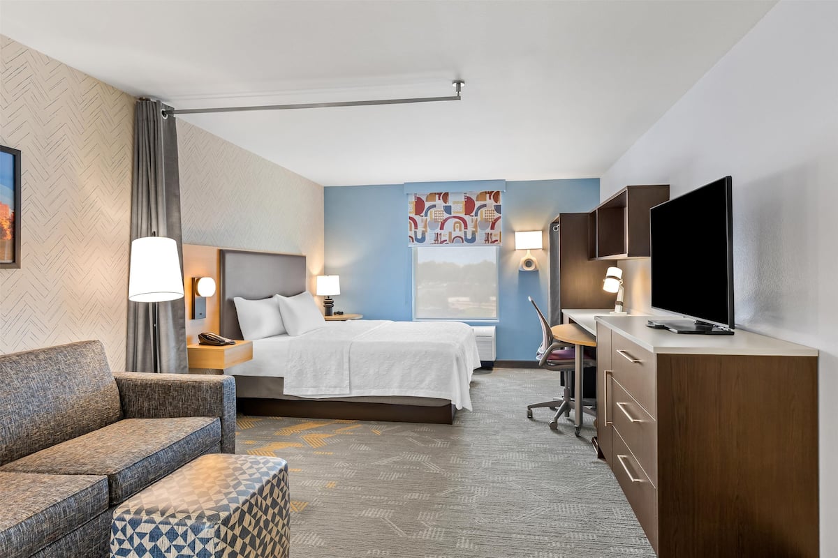 Ein Hotelzimmer mit einem Bett, einer Couch, einem Schreibtisch mit Fernseher und einer Schreibtischlampe.