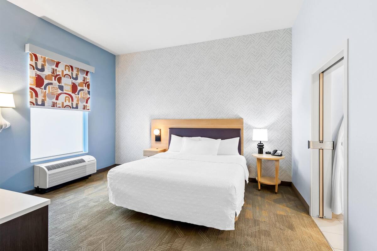 Ein Hotelzimmer mit einem großen Bett, einem Nachttisch mit Lampe, einer Wand-Klimaanlage und einer Wand mit Muster.