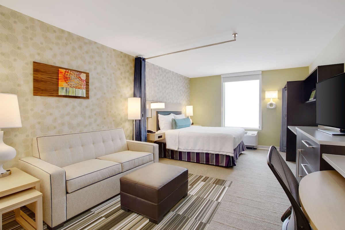 Quarto de hotel com cama, sofá, escrivaninha, cadeira e televisão.
