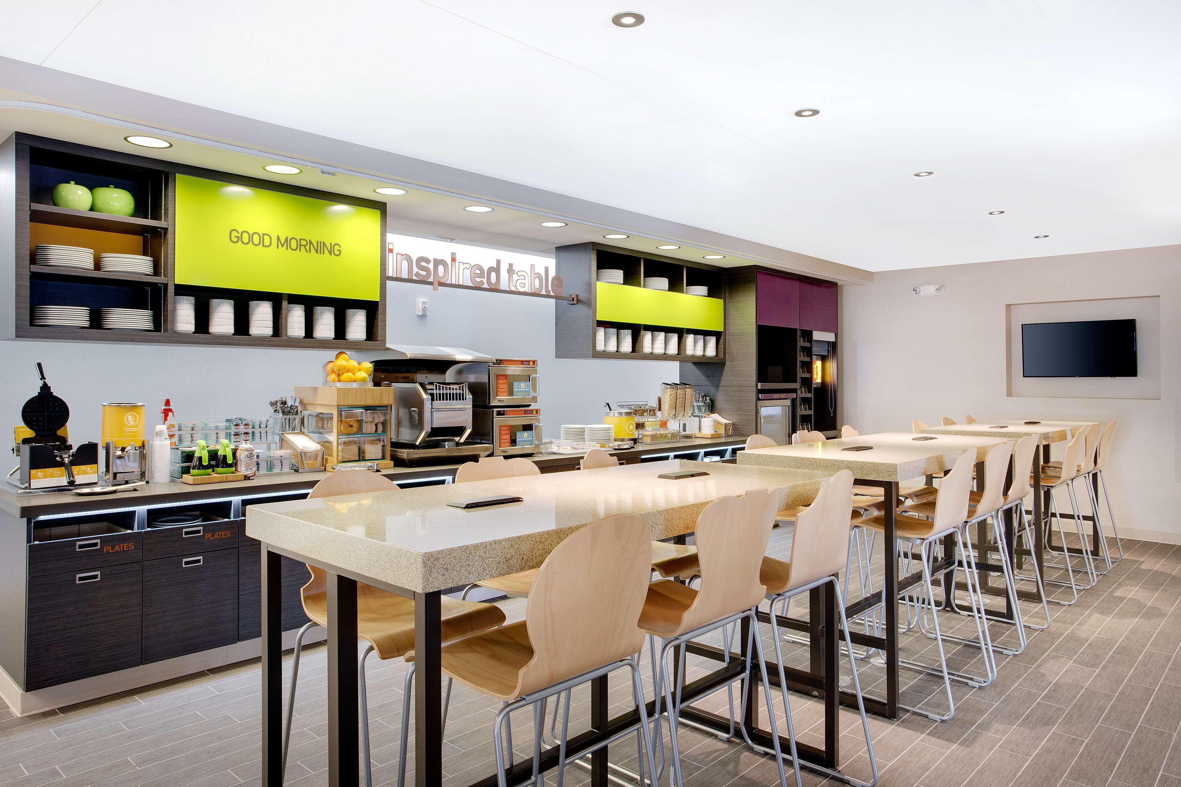 Un restaurante moderno con una barra larga, varias zonas de estar y una cocina a la vista.